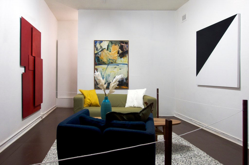 Documentation from the contemporary art installation In the Year Twenty Twenty One by Alex Gawronski held at KNULP gallery in Camperdown, Sydney, Australia. A contemporary art installation in the form of a fictional lounge room setting containing paintings, a sculpture, a blue vase with colorful flowers and contemporary magazines. These are roped off like a museum display.