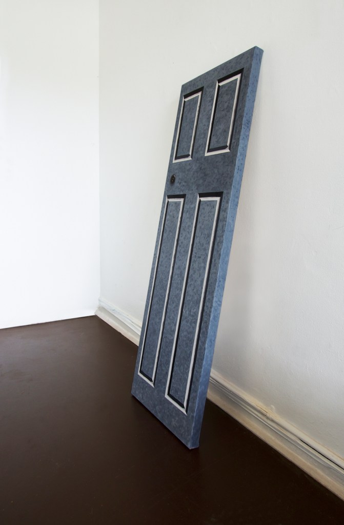 Grey painted door leaning against white wall on brown floor side on